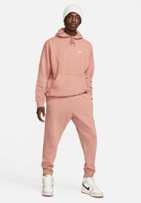 Pink fleece hoodie with a front pocket and drawstring, paired with matching jogger pants. Both feature a subtle speckled texture.