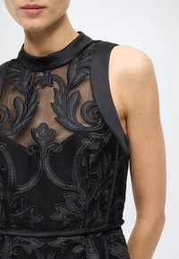 Black dress featuring a mesh bodice with intricate floral embroidery, a high collar, and satin accents on the shoulders.