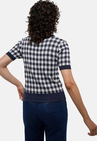 Haut en tricot à manches courtes à carreaux navy et blancs, avec un col et un ourlet ribbés, présentant une silhouette ajustée et une texture lisse.