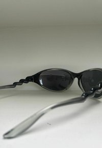 Zwarte zonnebril met een slank, rond ontwerp. Semi-transparant montuur met grijze accenten, donkere glazen en een gestructureerde poot.