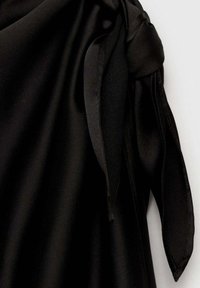 Tissu satin noir avec un long détail de nœud doux noué lâchement sur un fond blanc.