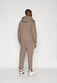 Brun hettegenser med kengurulomme og matchende joggebukser, med elastiske mansjetter og søm. Brukt med hvite og svarte treningssko.