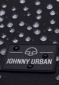 Textil negru cu picături de apă, având un etichete rectangulară cu logo-ul "JOHNNY URBAN" scris cu alb, cu accente negre.