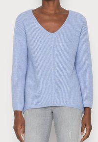 Light blue knit sweater with a V-neck, ribbed texture, long sleeves, and a relaxed fit, paired with light gray jeans.