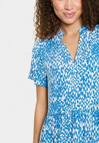 Kurzes Kleid in Blau und Weiß mit Kragen, gefaltetem Rock und einem strukturierten Muster aus abstrakten Formen.