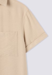 Camicia beige a maniche corte realizzata in tessuto testurizzato, con taschino sul petto e colletto classico. L'orlo è leggermente arrotondato.