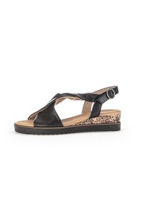 Sandale en cuir noir avec des lanières croisées, boucle réglable à la cheville et un talon compensé avec un motif léopard sur le côté.