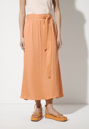 Jupe midi orange en tissu lisse avec une ceinture nouée à la taille, associée à des sandales à plateforme orange avec des brides de cheville.