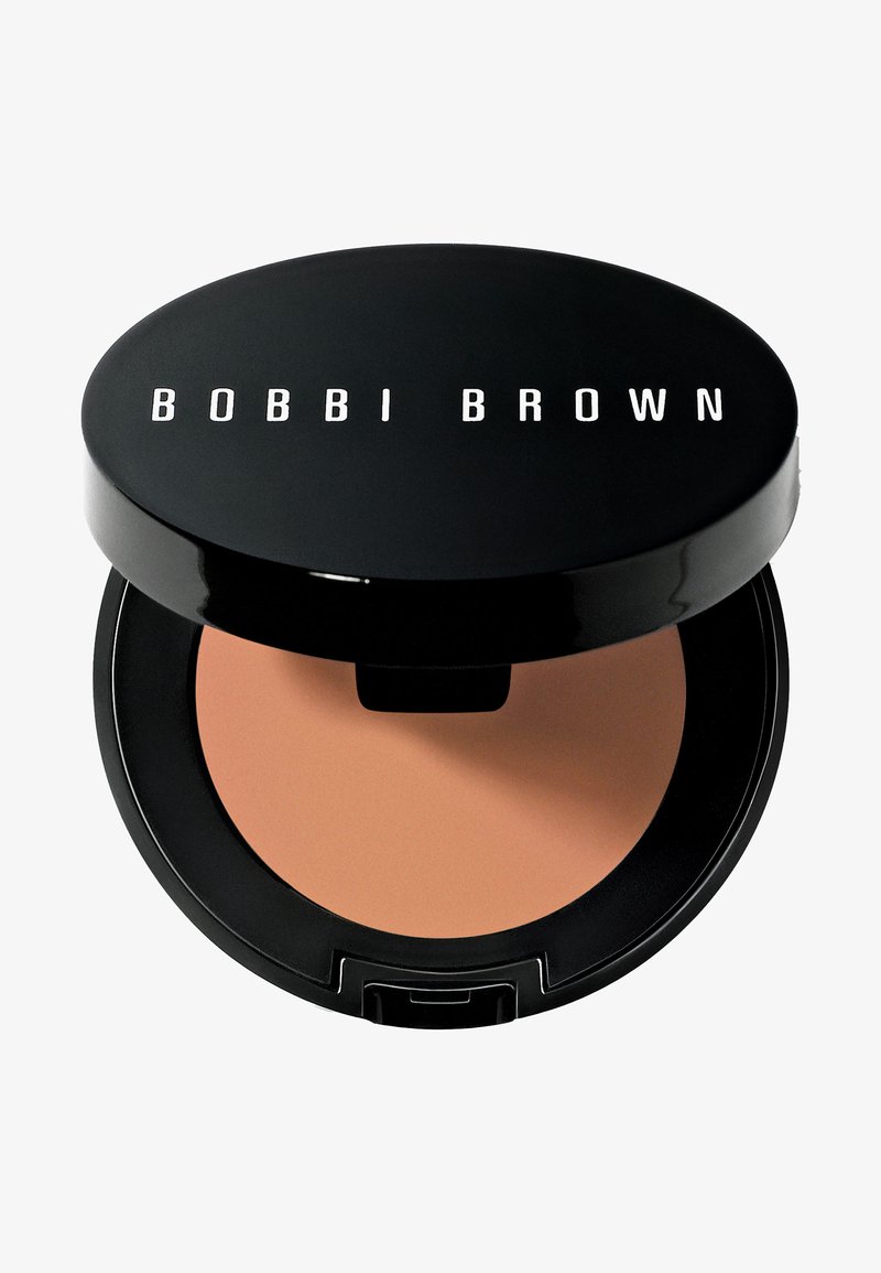 Poudre compacte dans un boîtier circulaire noir avec "BOBBI BROWN" imprimé en blanc. La poudre est d'une teinte beige clair avec une texture lisse.