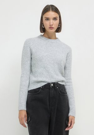 Pull en maille gris clair texturé avec un col rond et des manches longues, assorti à un jean noir taille haute avec poches latérales.