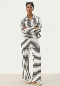 Ensemble de détente rayé en noir et blanc ; comprend un pull avec col zippé et un pantalon ample. Tissu doux avec une coupe décontractée.