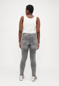 Sive skinny jeans z zbledelim pranjem, zelo visoko pasu, petimi žepi in gladko teksturo tkanine. Usklajene z belo majico brez rokavov.