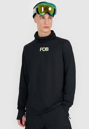 Młody mężczyzna w czarnej bluzce z długim rękawem z logo „FOB”, czarnych spodniach i odblaskowych goglach narciarskich spoczywających na czole, patrzący lekko w prawo.