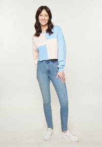 Felpa cropped in blu chiaro e rosa con maniche oversize; abbinata a jeans aderenti chiari e sneakers bianche. Tessuto soffice.