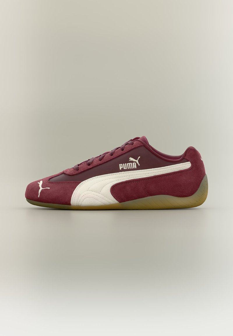 Μπορντό αθλητικό παπούτσι Puma με λευκή ρίγα, σουέντ υφή, σχέδιο με κορδόνια και καουτσούκ σόλα, εμφανιζόμενο σε πλευρικό προφίλ σε απλό φόντο.