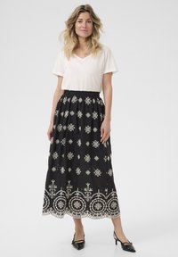 Zwarte, geborduurde maxi-rok met witte bloempatronen en een scalloped zoom, gecombineerd met een eenvoudige, losse crème V-hals T-shirt.