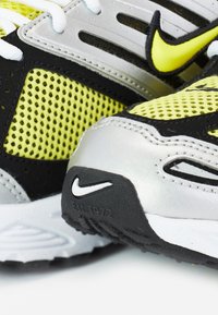 Nærbillede af gule og sorte Nike-sneakers med netstof, hvide snørebånd og synlige Nike-logoer på tå- og sidepaneler.