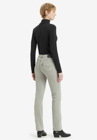 Jeans de mezclilla gris de pierna recta con una cintura de media altura y bolsillos traseros con un logotipo bordado distintivo. Llevados con una blusa negra de manga larga.