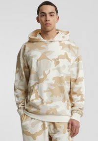 Beige kamuflasje hettegenser laget av en myk bomullsblanding, med kengurulomme, snorhette og ribbede mansjetter for en komfortabel passform.