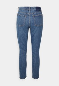 Jeans de denim azul de corte slim, de cintura média, com uma textura suave, cinco bolsos e detalhes de costura discretos na parte de trás.