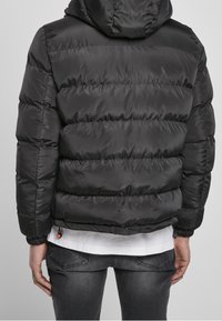 Czarna kurtka puchowa z kapturem, z poziomym przeszyciem, elastycznymi mankietami i sznurkiem na dole, umożliwiającym regulację dopasowania.