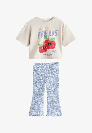 Tricou bej cu grafică colorată de măr și text. Pantaloni evazați albaștri cu model floral alb. Material moale, design casual.