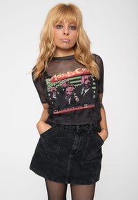 Black sheer shirt with a graphic design featuring a red and green "Mötley Crüe" print, paired with a high-waisted black denim skirt.