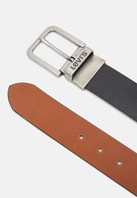 Zwarte en bruine leren riem met een zilveren metalen gesp met het "Levi's" logo; gladde textuur met gaatjes aan de bruine kant.