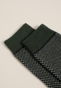 Stickade strumpor med grön mudd och ett svartvitt geometriskt mönster. Har ribbat mönster upptill och slät yta på resten.