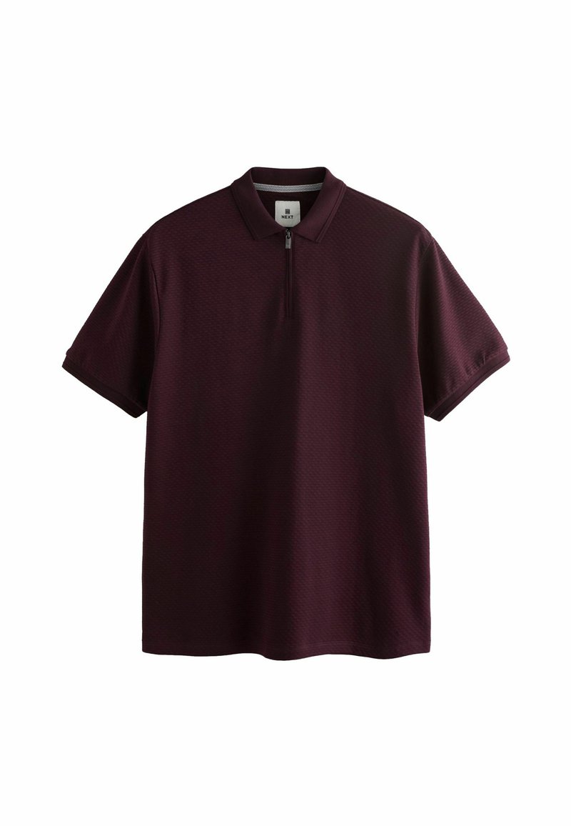 Polo cu mânecă scurtă de culoare burgundă, cu guler cu fermoar, material texturat și croială lejeră. Dispune de o etichetă cu numele brandului în interior.