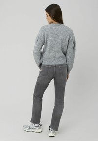 Pull en maille gris avec une finition texturée, doté d'un ourlet côtelé, associé à un jean gris slim et des baskets argentées.