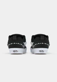 Černobílé tenisky s nízkým profilem, texturovanou tkaninou, s hřebíkovými detaily na zadní straně a bílou gumovou podrážkou s logem.