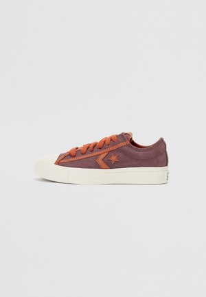 Baskets basses en daim violet sourd avec lacets orange et logo étoile, semelle en caoutchouc blanche, vue de côté sur fond uni.