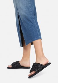 Zwarte geweven leren instapsandalen met een platte zool; gedragen met een blauwe denim midi-rok met een voorste split.