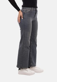 Jeans a zampa d'elefante in denim scuro con un finish sbiadito e design a cinque tasche. Indossati con sneakers bianche con accenti neri.