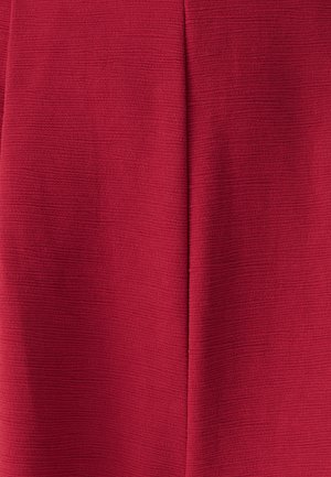 Detailný záber na textúrovanú červenú látku so stredným vertikálnym švom a viditeľným vzorom tkania.