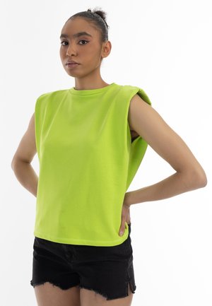 Limegrøn ærmeløs top lavet af bomuld, med en rund halsudskæring og løs pasform, parret med sorte denimshorts med rå kant.