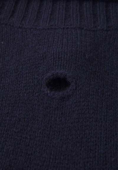 Mørk marineblå strikket stoff med et lite rundt hull i midten, som viser slitt eller skadet tekstur.