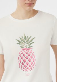 White t-shirt featuring a pink pineapple graphic decorated with green accents and a diamond pattern; text "Paradise Club" below the design.