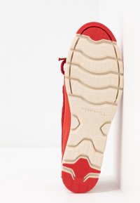 Semelle de chaussure de sport rouge avec bande de roulement blanche et rouge, motif de grip texturé, et nom de marque « Tamaris » visible en dessous.