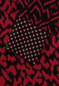 Röd och svart mönstrad tyg med en kantig design och texturerade element, kompletterad av en prickig manschett i kontrasterande färger.