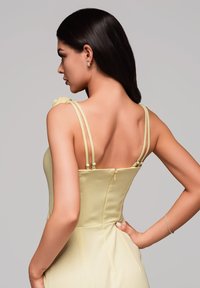 Robe en satin jaune avec de fines bretelles, présentant un corsage ajusté, une fermeture éclair au dos et une texture lisse. De fins accents et des détails de design subtils sont visibles.