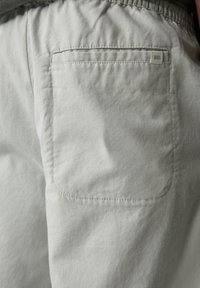 Shorts gris clair avec une taille élastique et une poche arrière ornée d'une petite étiquette logo. Le tissu a une texture lisse et douce.
