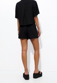 Camiseta negra recortada con mangas cortas combinada con pantalones cortos negros y sandalias gruesas con plataforma. Tela lisa y diseño minimalista.