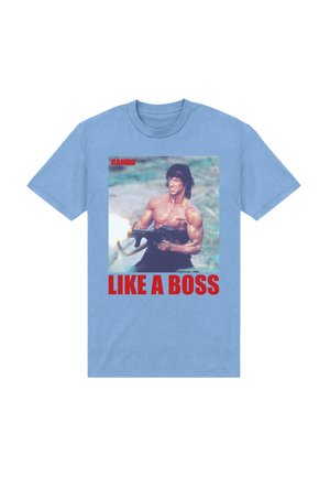 Lyseblå t-shirt med en bar overkrop muskuløs mand, der skyder med en maskinpistol og rød tekst med "RAMBO" og "LIKE A BOSS."