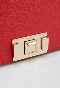 Rød tekstureret lædertaske med en guldtonet metal lukning med firkantede og rektangulære accenter samt "Furla" gravering.