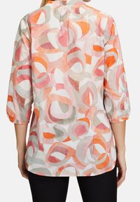 Kevyt, kuvioitu paita, jossa on abstrakteja pyörteitä vaaleanpunaisen, oranssin ja harmaan sävyissä, kolmannes hihoista ja pyöreä helma.