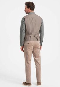 Beige Weste mit tailliertem Design, Rückenschnalle, kombiniert mit Cordhosen in einem helleren Beigeton und Wildlederschuhen.