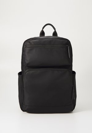 Un sac à dos noir en tissu lisse avec une poignée supérieure, deux poches zippées à l'avant et une poche latérale pour un rangement supplémentaire.