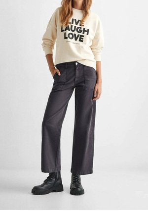 Felpa crema con scritta nera "LIVE LAUGH LOVE", abbinata a pantaloni neri a gamba larga e stivali neri con lacci. Tessuto a finitura liscia.